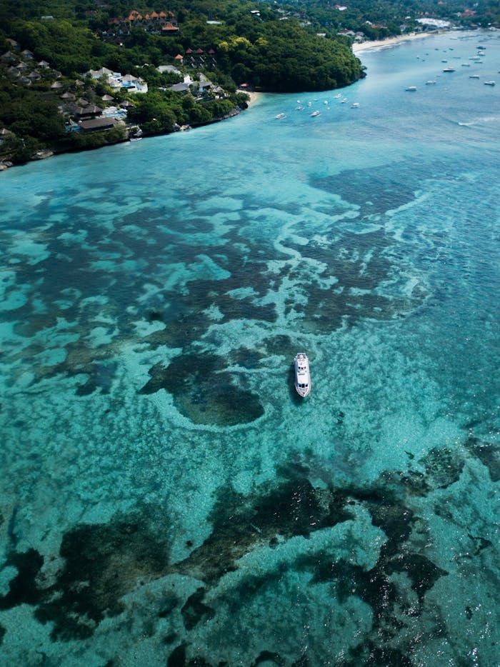 A scenic aerial shot of the vibrant coral reefs in Bali, featuring a boat navigating clear turquoise waters.